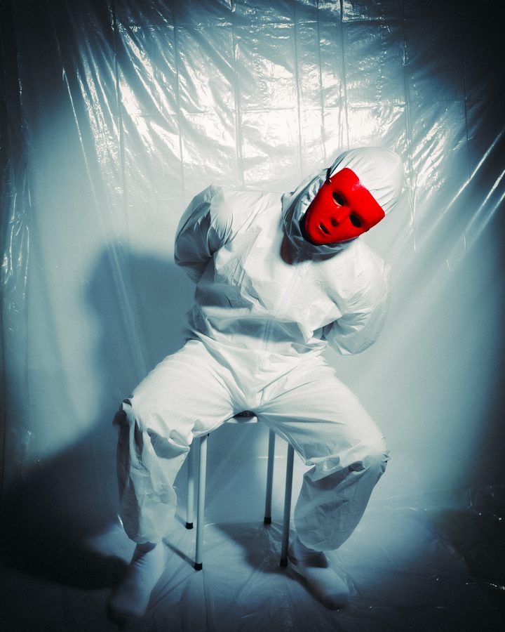 Figure in a white suit and red mask against a reflective backdrop